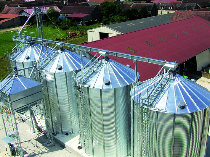 vue aérienne de 4 silos a grain avec convoyeur à chaine et boisseau a coté d'un hangar de stockage