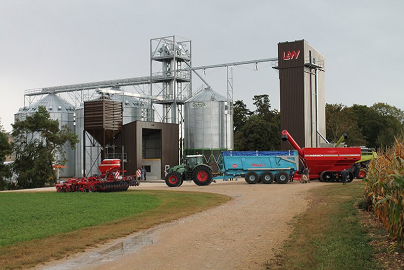 deux silos à grains fond plat un silo fond conique un boisseau et un séchoir LAW à économiseur d'énergie avec tracteur remorque transbordeur devant