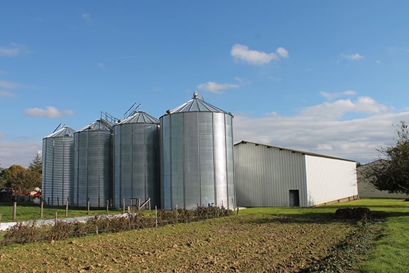 4 silos a grain alignés a coté d'un hangar de stockage