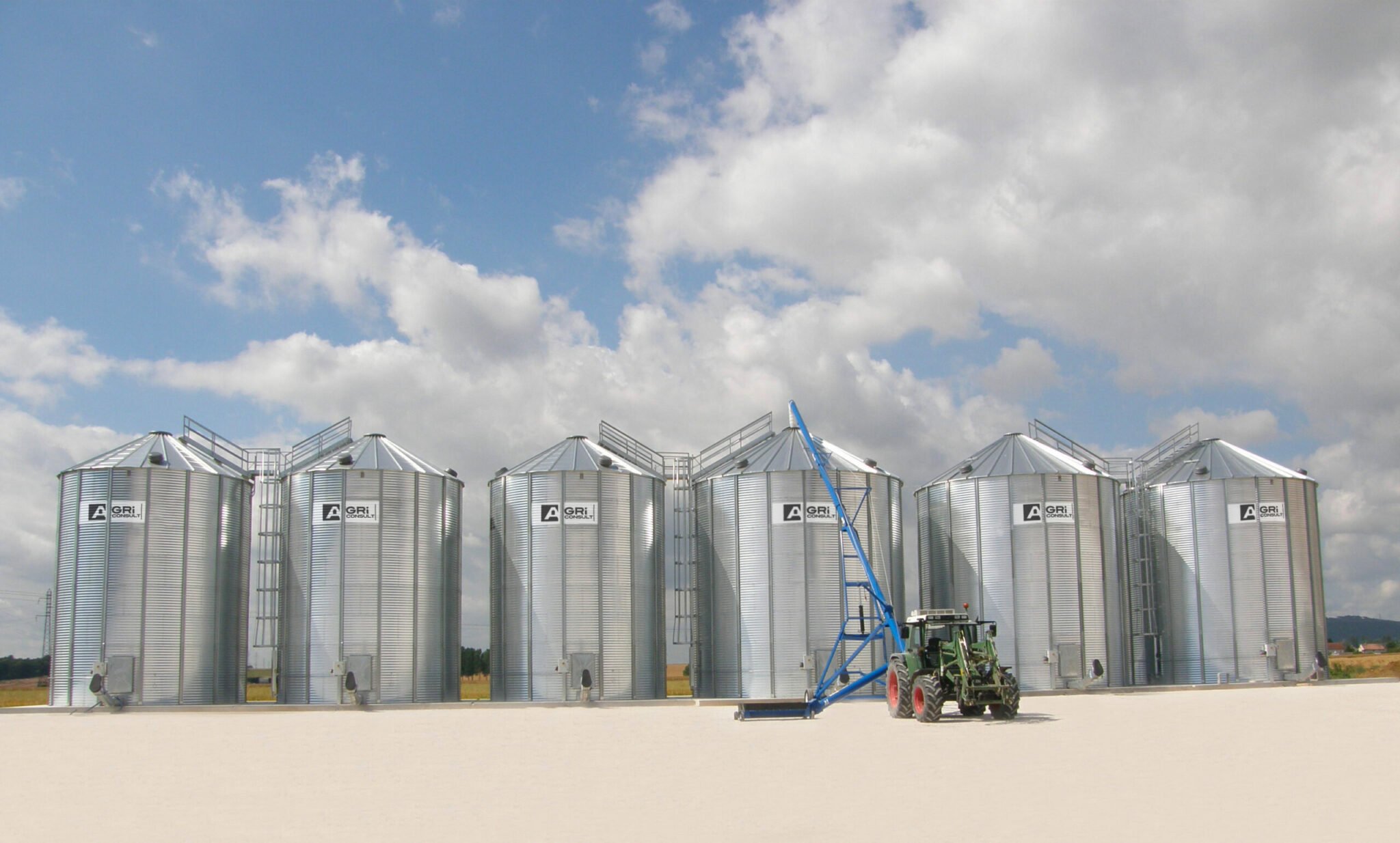 tracteur vu de face avec vis sur chariot swing away devant 6 silos à grains fond plat